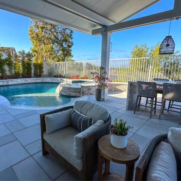 Freeform Swimming Pool with Neutral Stone and Beach Entry and Adjacent Outdoor Living Area